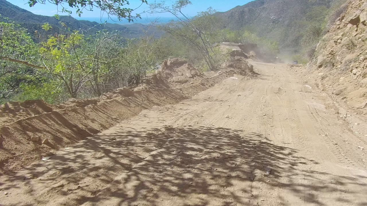 Unpaved road curving through rocky desert hills with dust ahead.