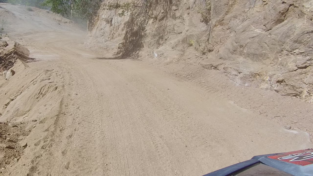 Dusty road curves left between rough earth walls and scrub.