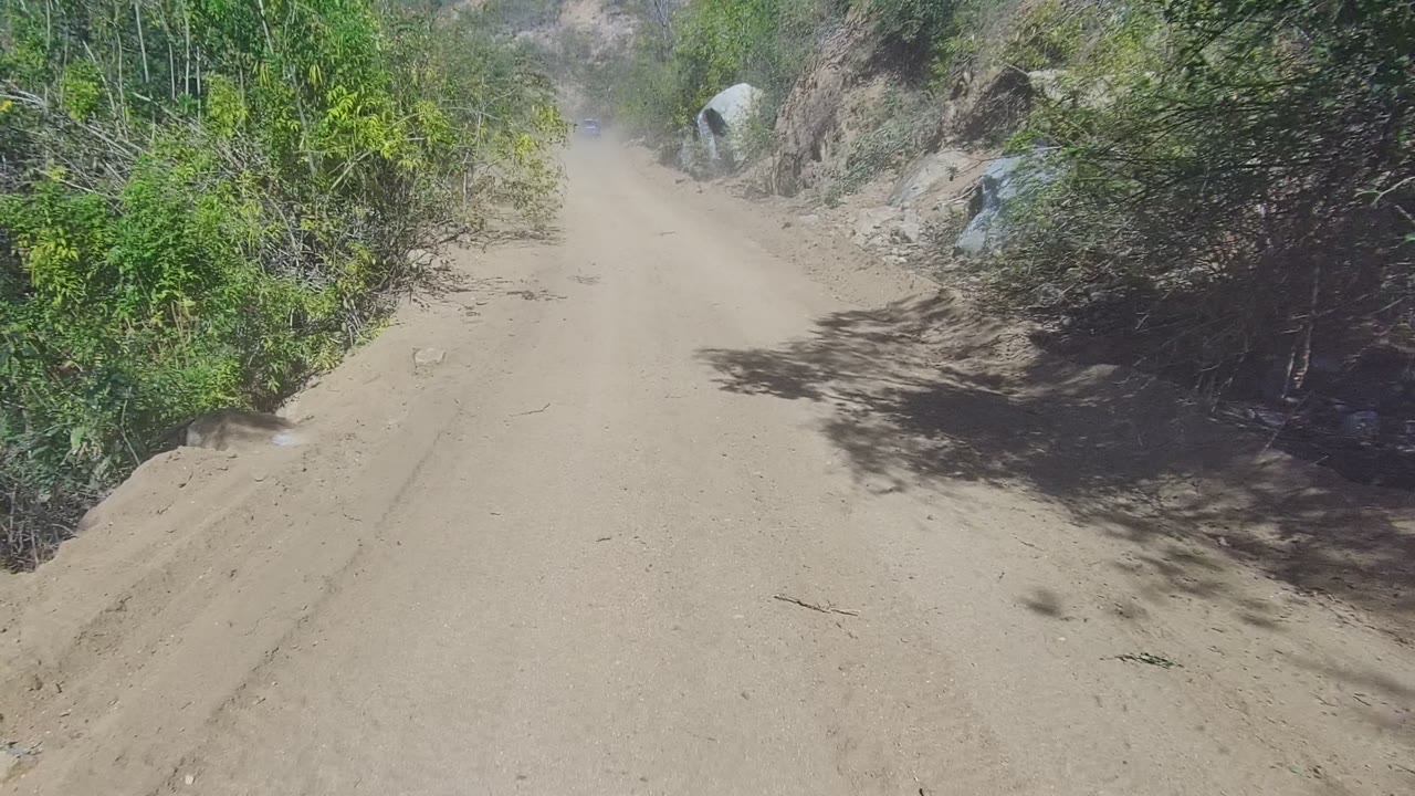 Sandy road beside brush and rocky hillside