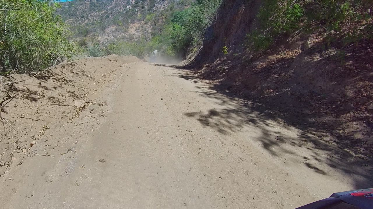 Dusty mountain dirt road curving past scrub and exposed rock.