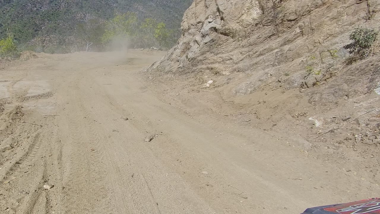 Dusty dirt road in Los Cabos, Baja California Sur curving beside a rocky slope with tire marks, brush, and no visible people.