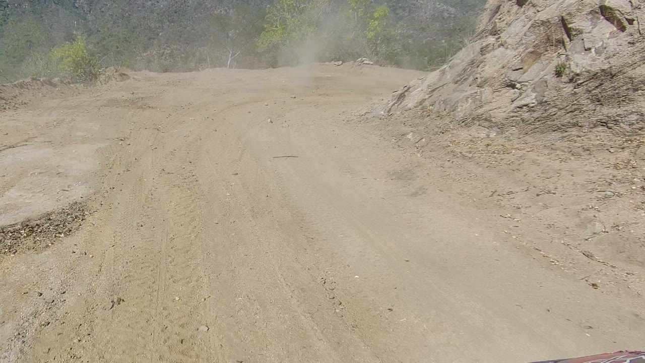 Vehicle view over a dusty road between rocky hills