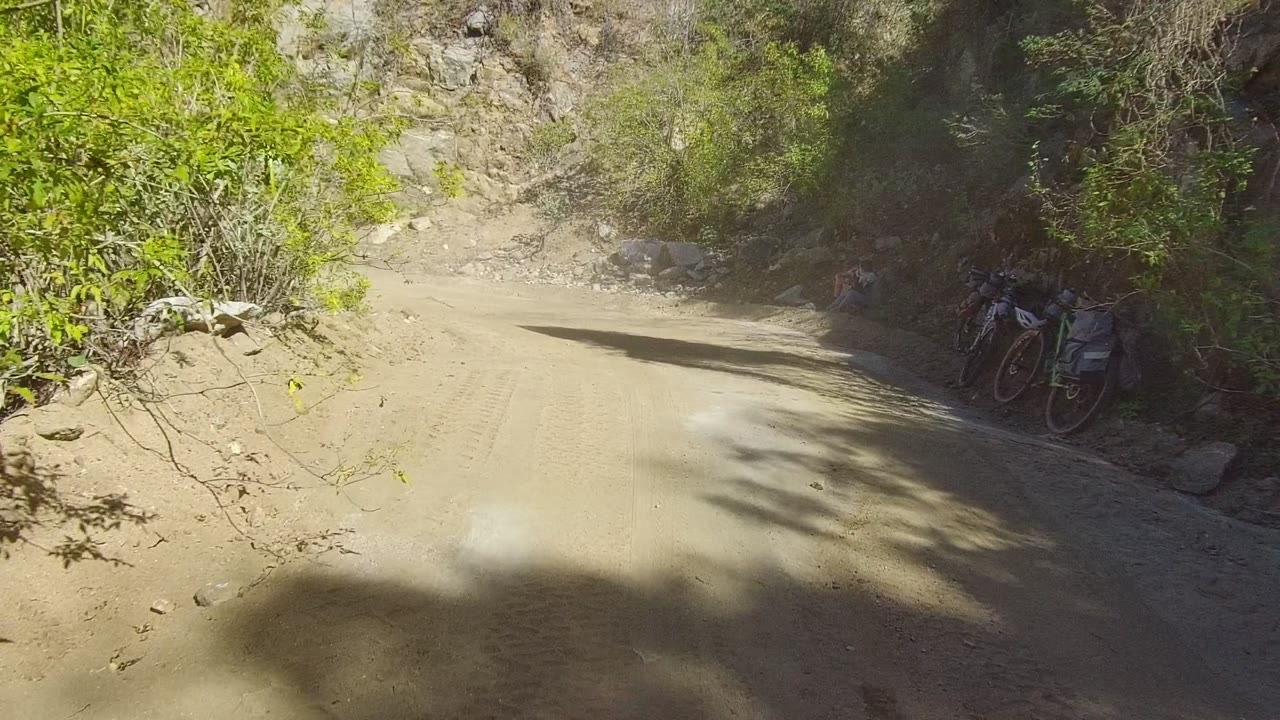 Dusty dirt road in Los Cabos, Baja California Sur, Mexico, curving through rocky brush with tree shadows across the track and no visible people.