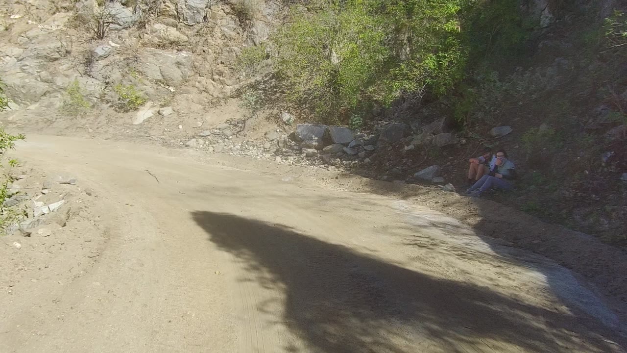 Pale dirt road bordered by rocky hillside and brush