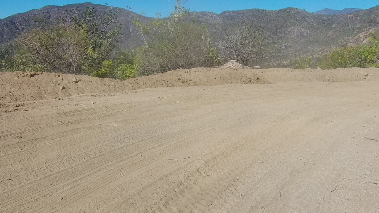 Dirt road curving near green brush and rocky mountain slopes