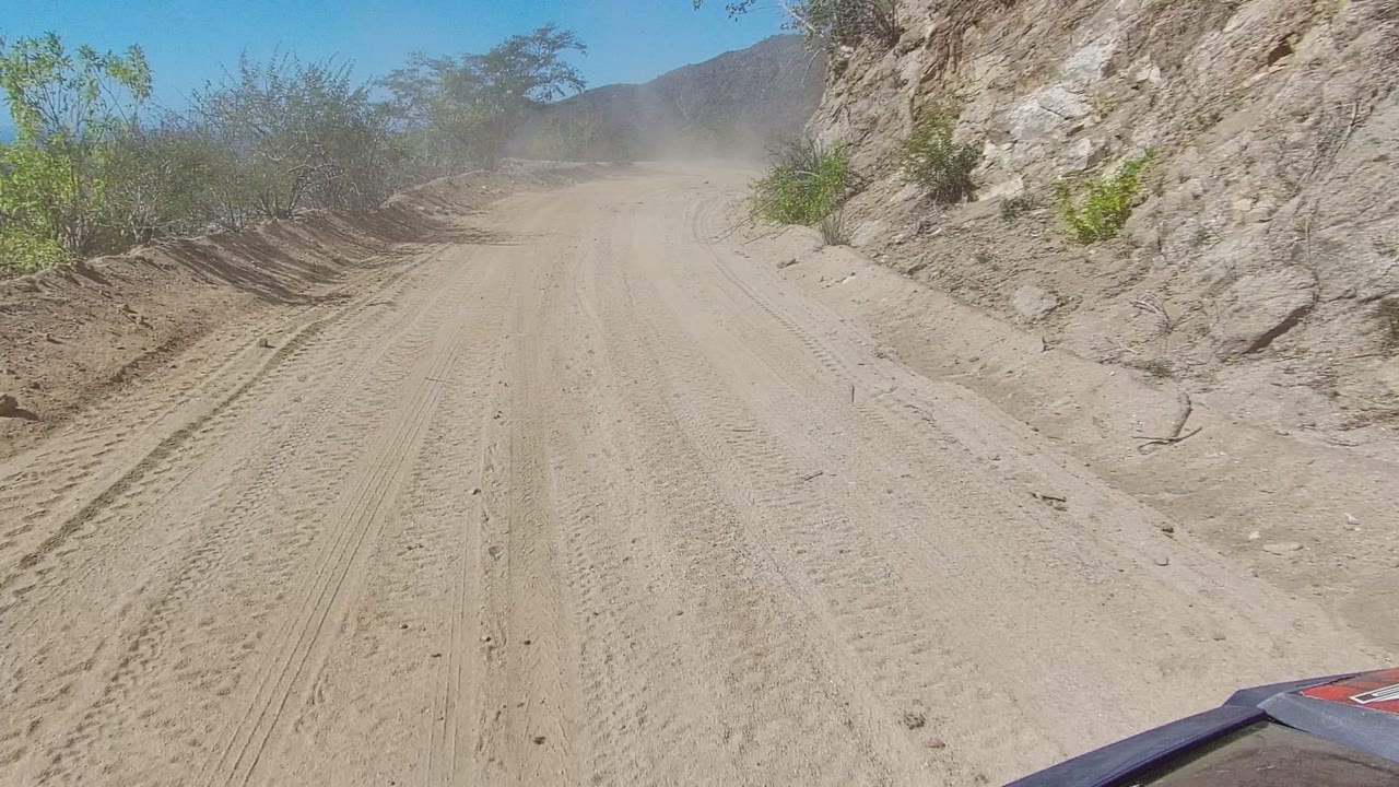 Forward view down a sandy mountain road with dust ahead.