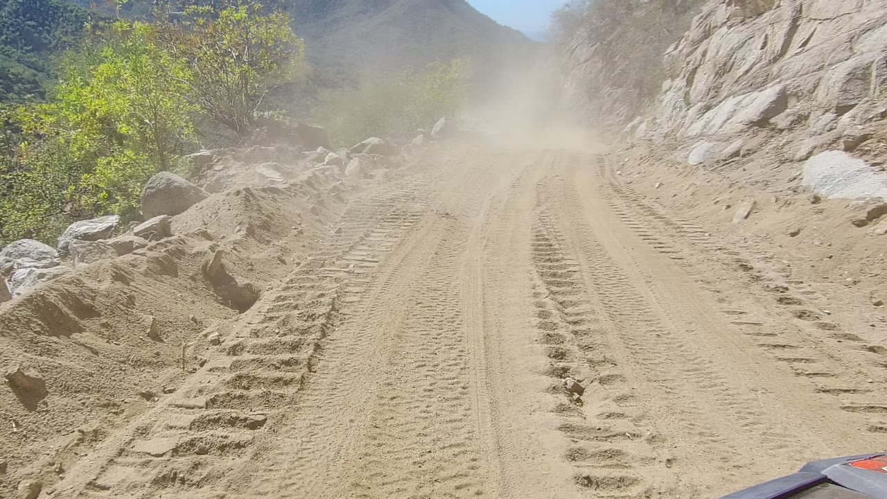 Sandy road with parallel tire marks and dust ahead near rocks.