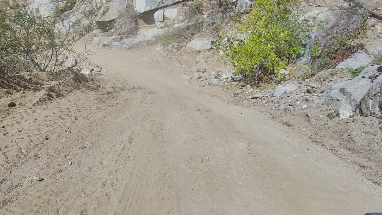 A closer point on the Los Cabos dirt road shows a raised pile of sand and gravel beside a rock face, sparse greenery, and no visible people.