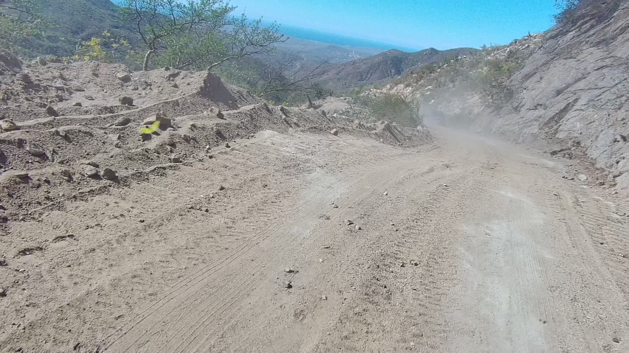 Rocky roadside with dirt track, shrubs, and distant blue horizon