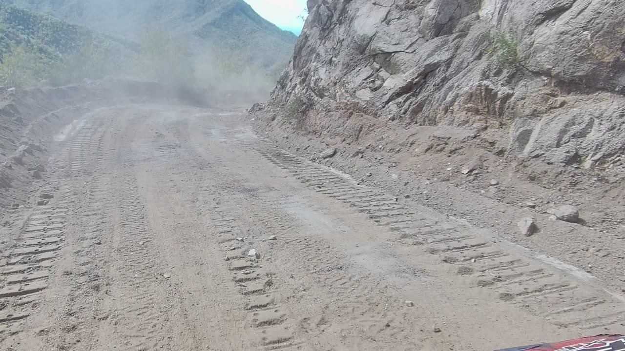 Dust hangs over a rutted dirt road in Los Cabos as the track runs forward between rocky slopes, with no visible people in the frame.