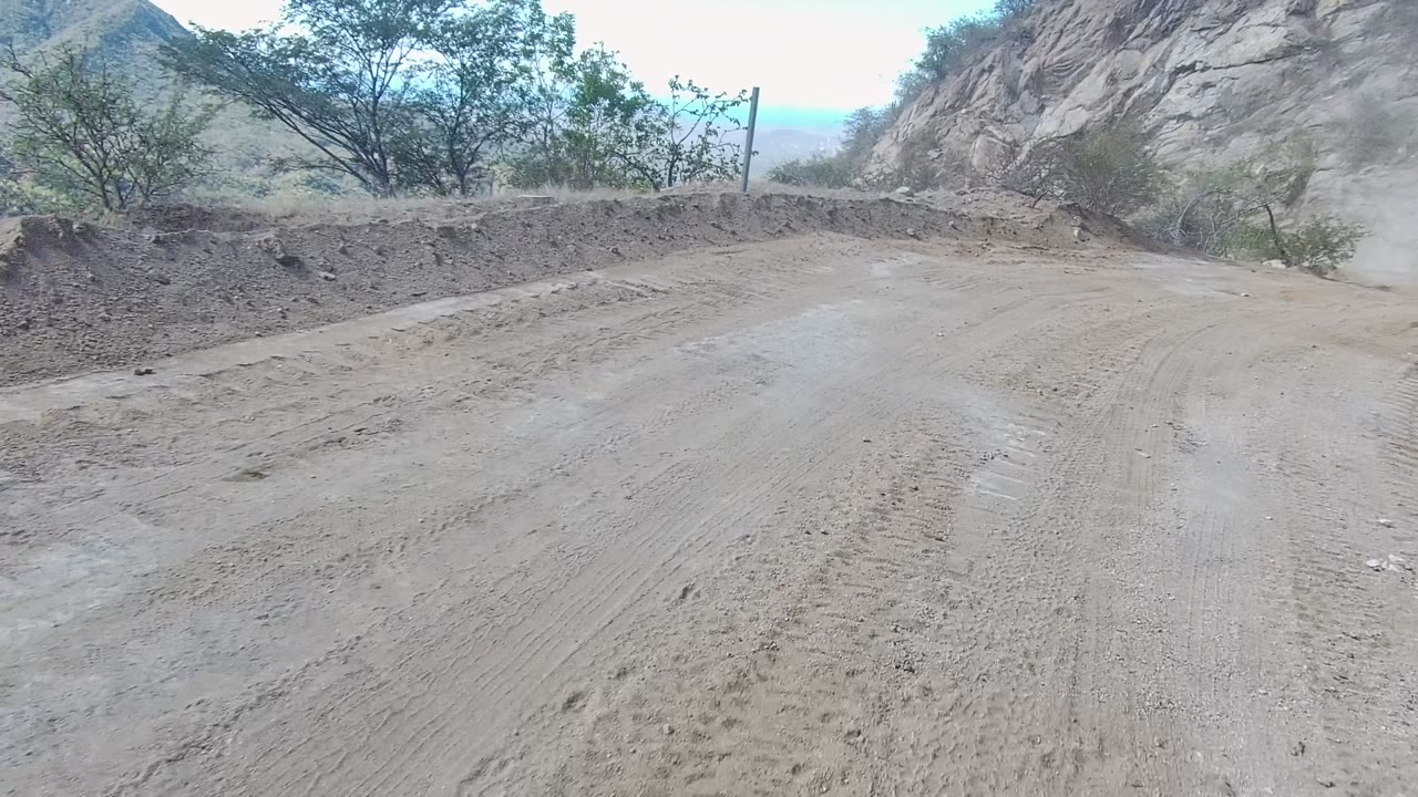 Opening view of a pale dirt road curving through rocky terrain in Los Cabos, Baja California Sur, with sparse vegetation, tire tracks, and no visible people.