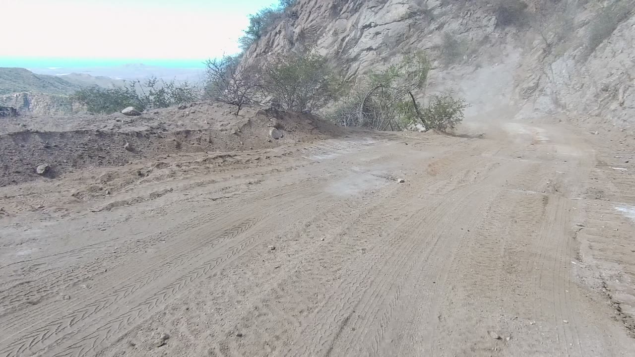Dirt road bordered by a steep rock wall with dust over the track.