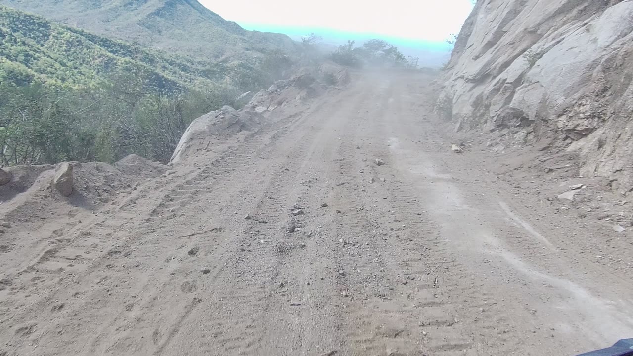 Unpaved road climbing between rock face and scrubby hillside