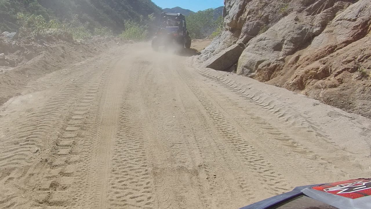 Vehicle farther ahead on rutted dirt road beside rocky slope.