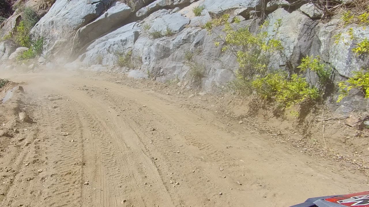 Opening frame of a sandy off-road trail in Los Cabos with tire tracks, pale rock walls, scattered shrubs, and no visible people.