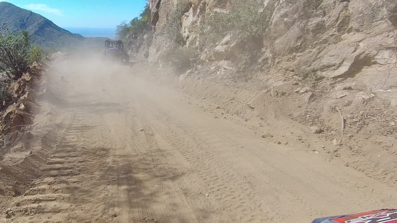 Sandy rutted road beside rock wall with dust ahead