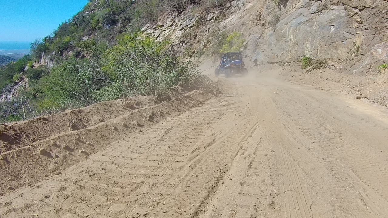 Off-road vehicle raising dust beside rocky hillside