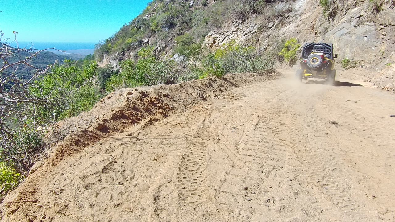 Off-road vehicle farther down a dusty dirt road on a rocky hillside.