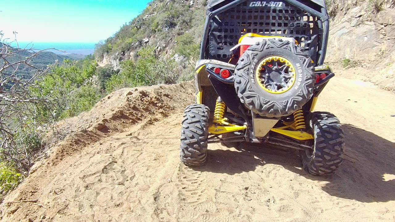 UTV rear tires climbing over rutted dirt on a mountain road