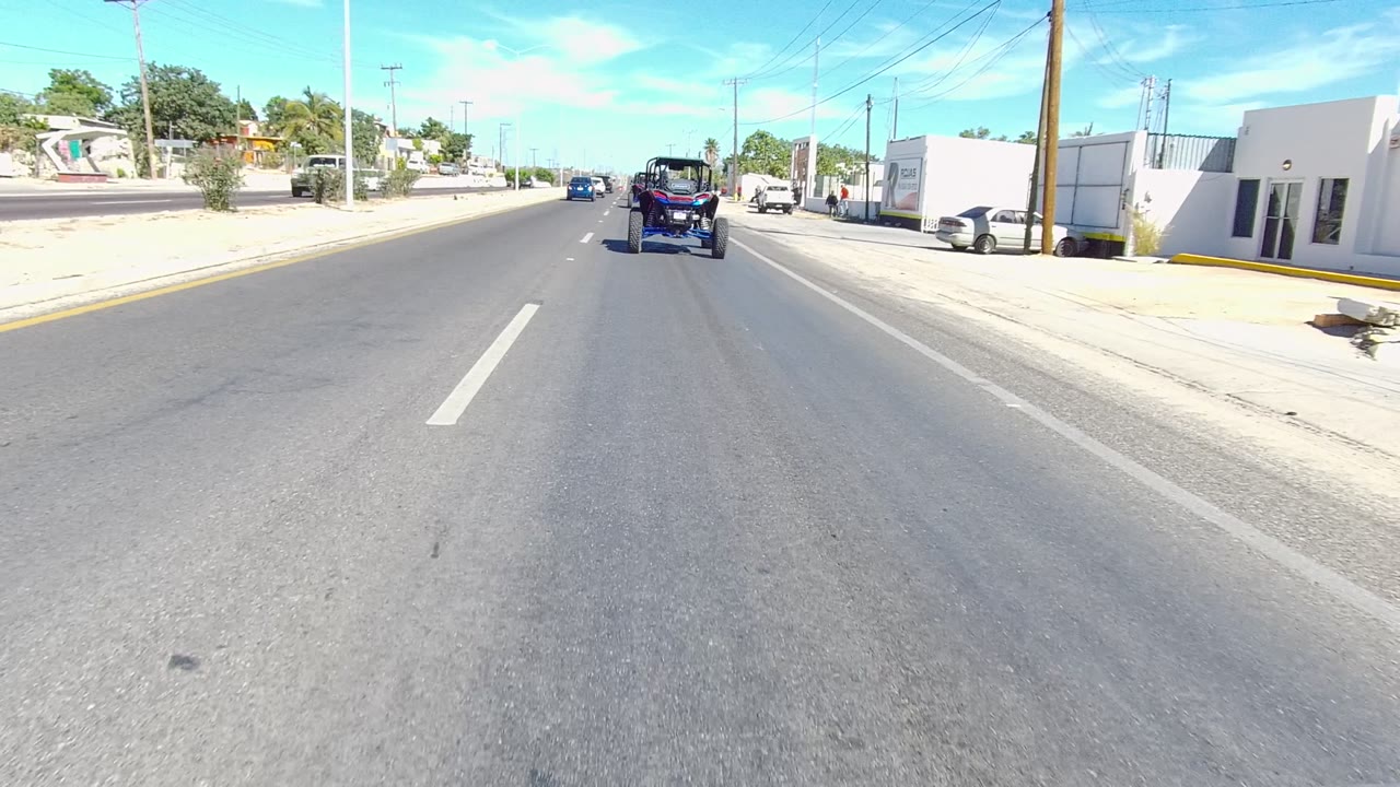 Roadway view with a dark off-road vehicle ahead, white building, and parked cars.