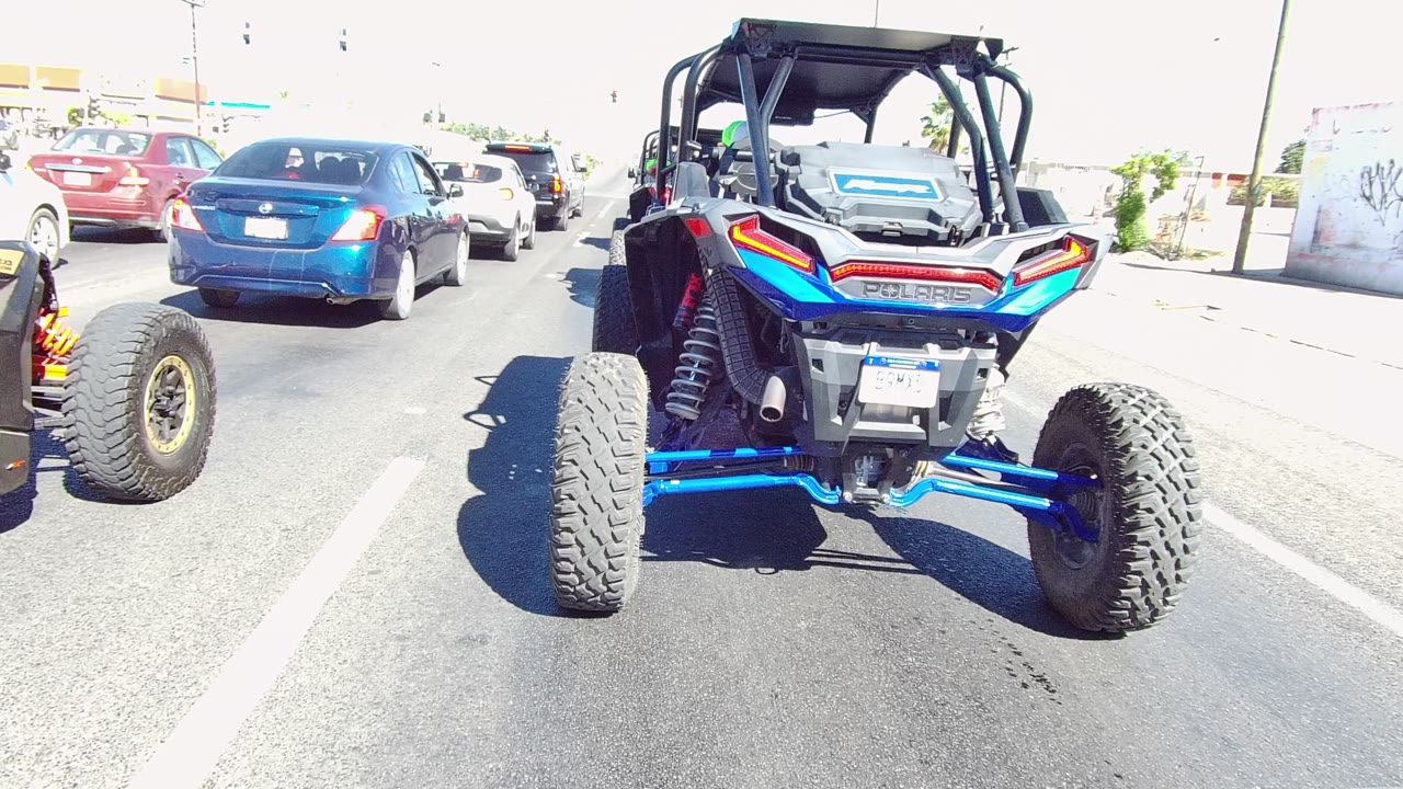 A close rear view shows the blue and black UTV's angular red tail lights and wide tires in Los Cabos traffic, with no visible people in frame.