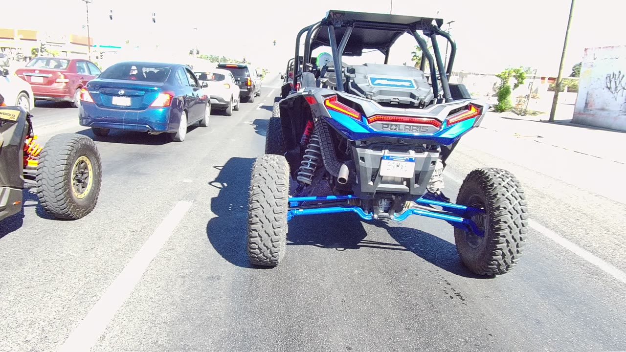 Rear view of a blue and orange UTV in traffic beside cars on a sunny road.