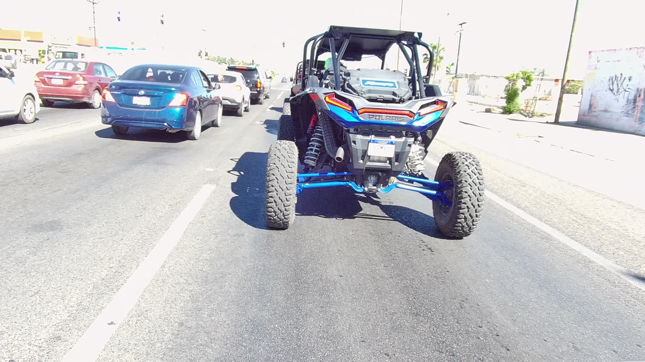Blue UTV and cars continuing along a sunny road
