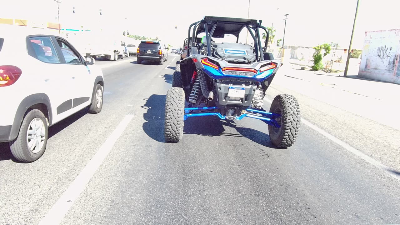 White car passing beside a blue UTV on a sunny road.