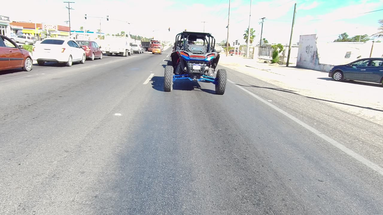Blue UTV ahead in the roadway with white and red cars in traffic.