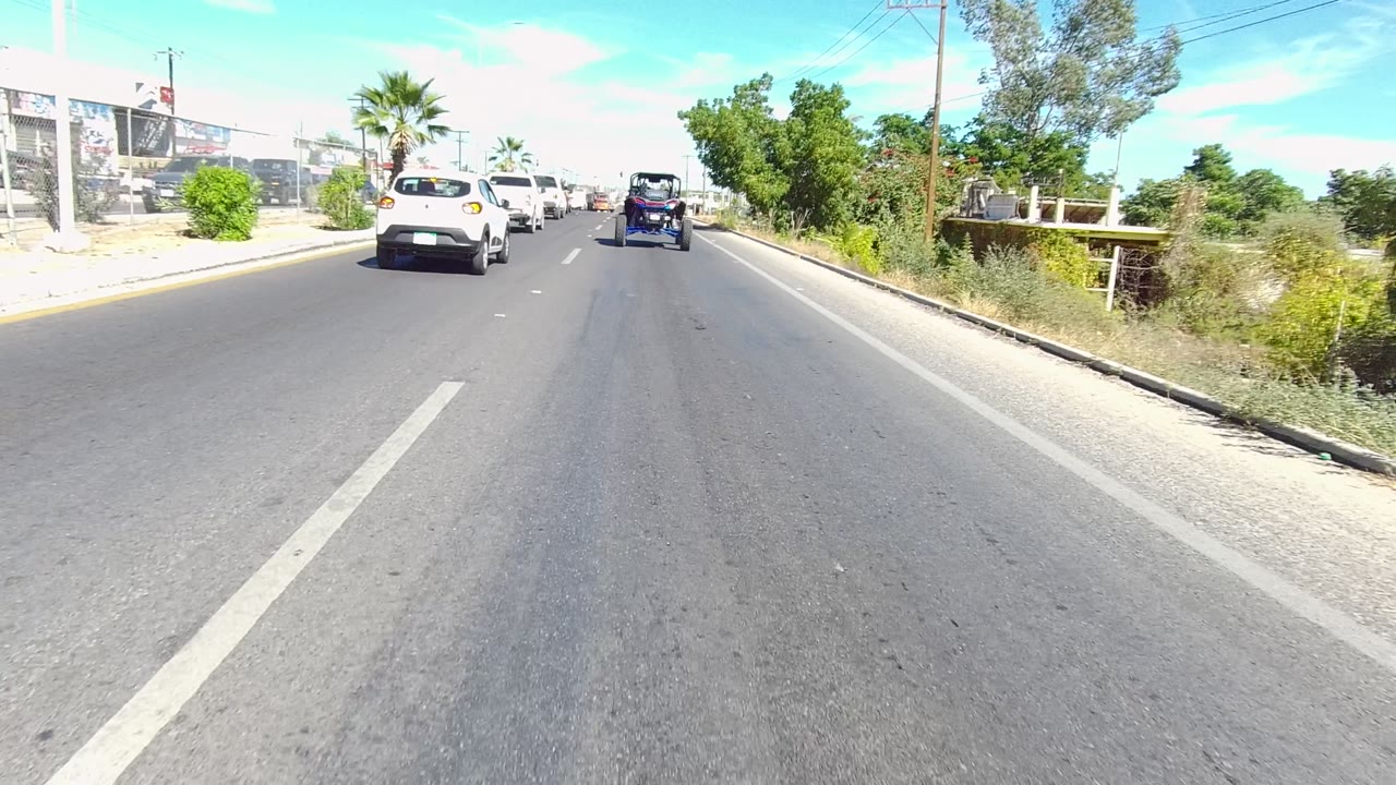 Third frame in Los Cabos shows the white car closer in the left lane area, a dark vehicle ahead, roadside greenery to the right, and no visible people.