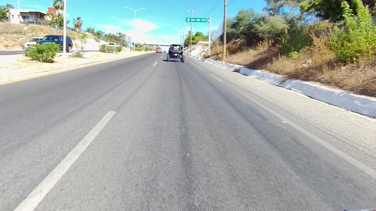 Paved road approaching an intersection area with a vehicle ahead and hillside vegetation.