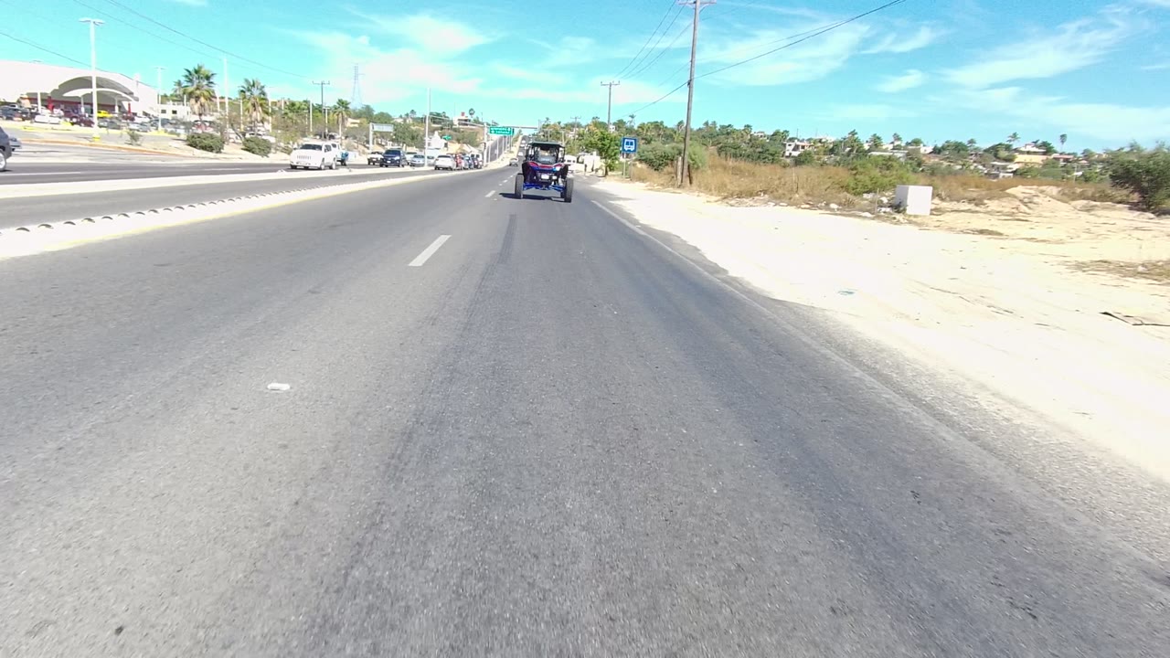 Sunny roadway with a dark vehicle ahead and traffic in the opposite lanes.