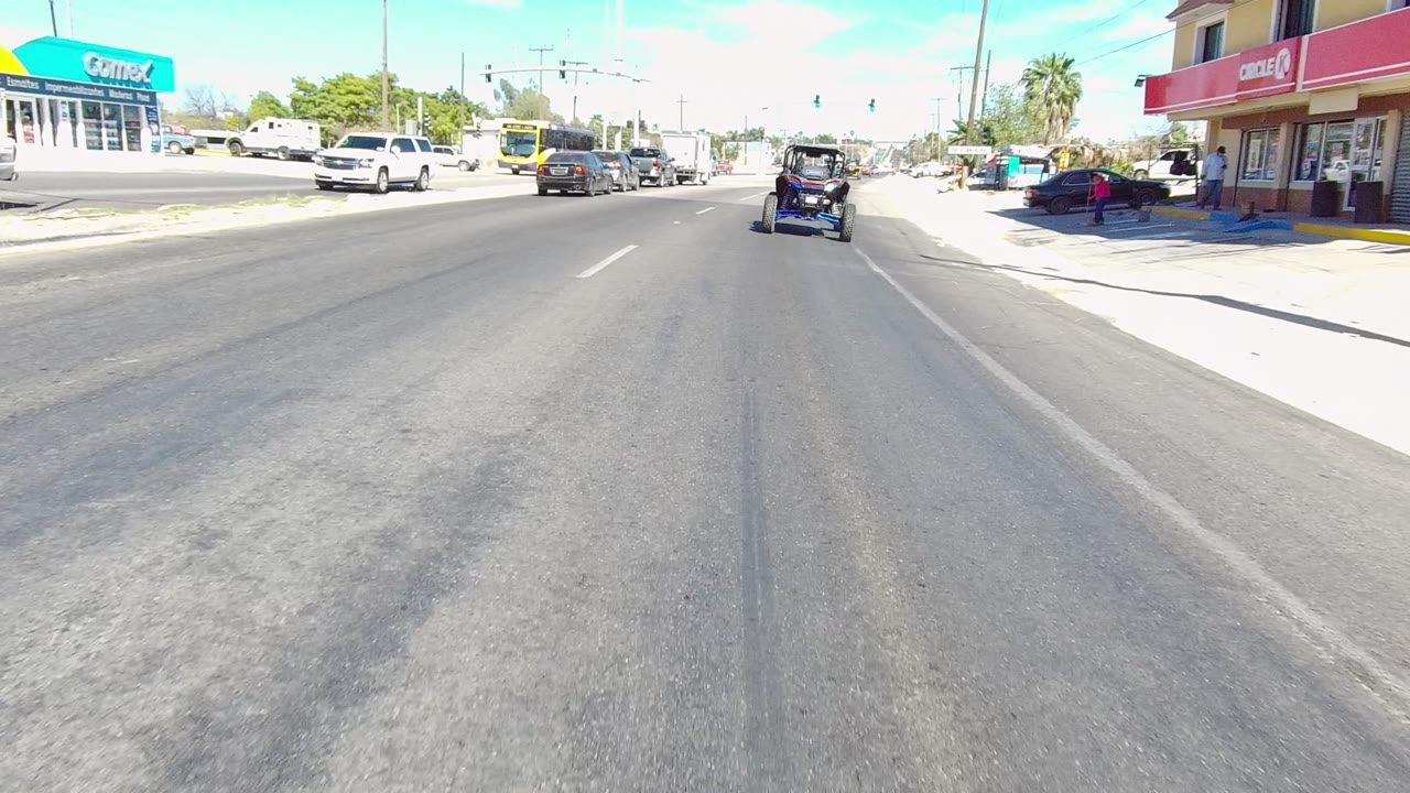 Golf cart continues toward an intersection with cars, a bus, and storefronts nearby.