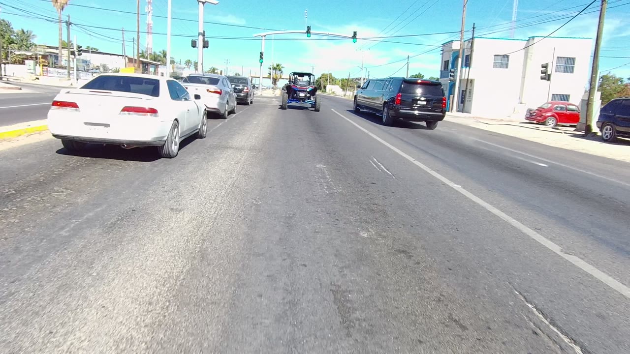 White sedan and black SUV driving near a signalized urban intersection.