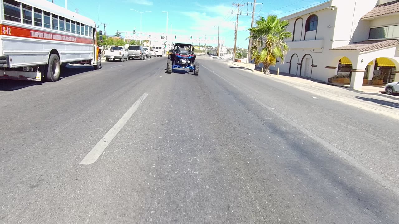 Bus beside a small open-top vehicle on a sunny multi-lane road