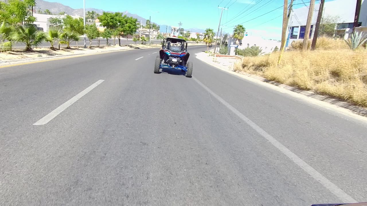 Blue dune buggy farther ahead on a wide road with dry roadside landscaping.