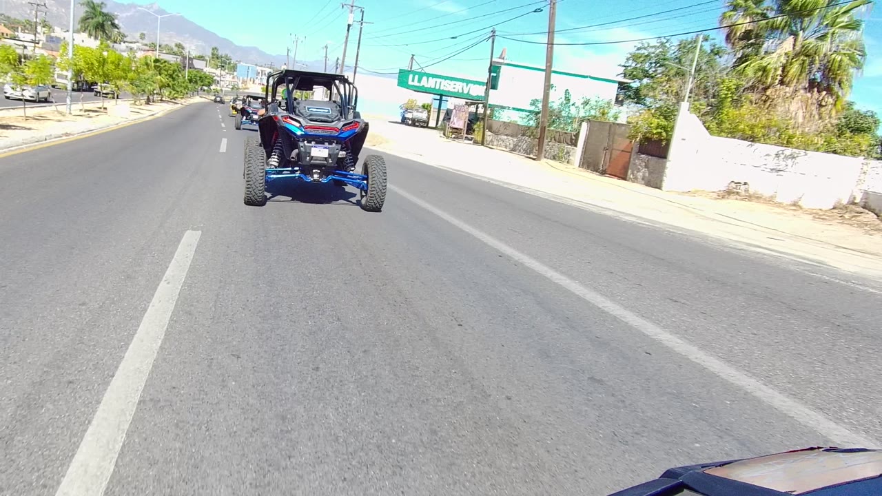Blue dune buggy centered on a paved road near palm trees and storefront signage.