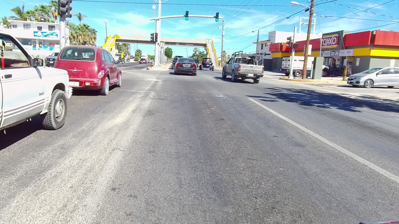 A red car and pickup trucks move near a storefront-lined intersection.