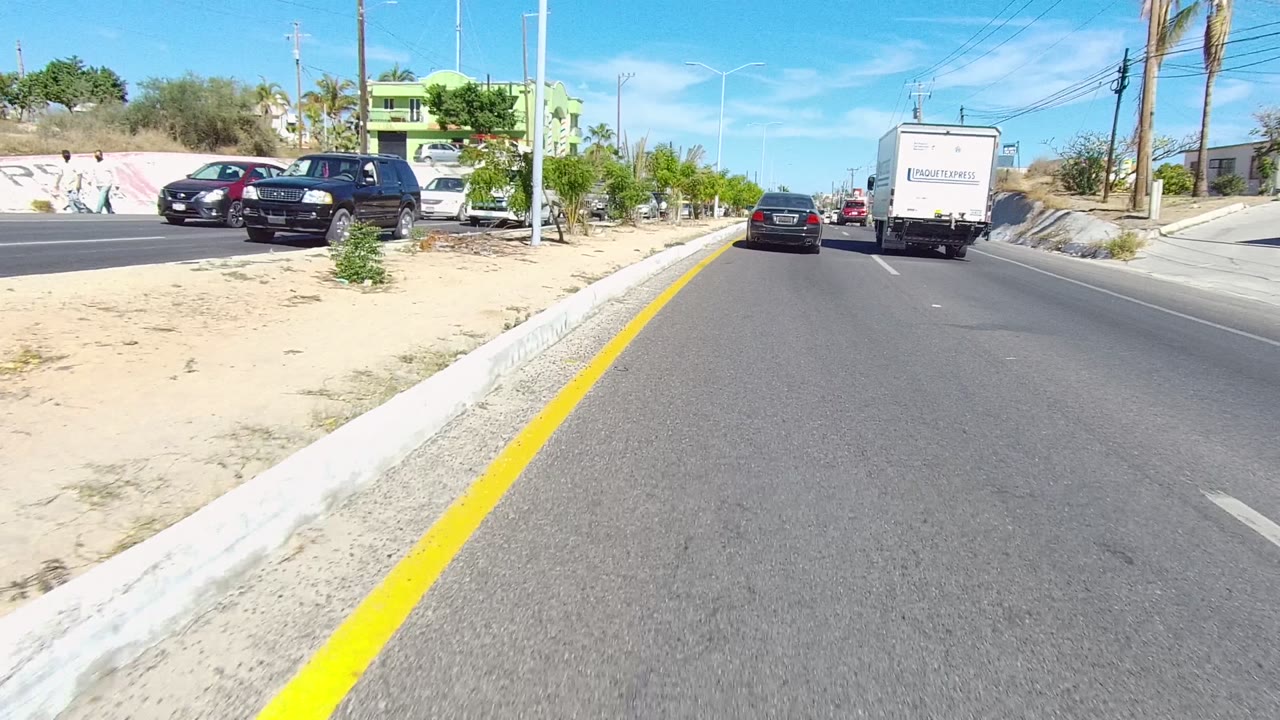 Roadside sand, parked cars, and a white delivery truck ahead