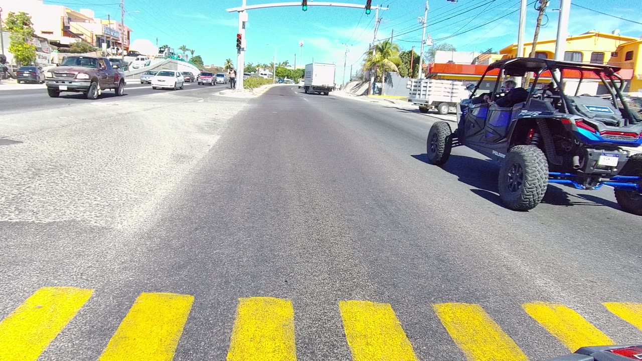 Blue off-road vehicle enters the intersection near cars and storefronts.