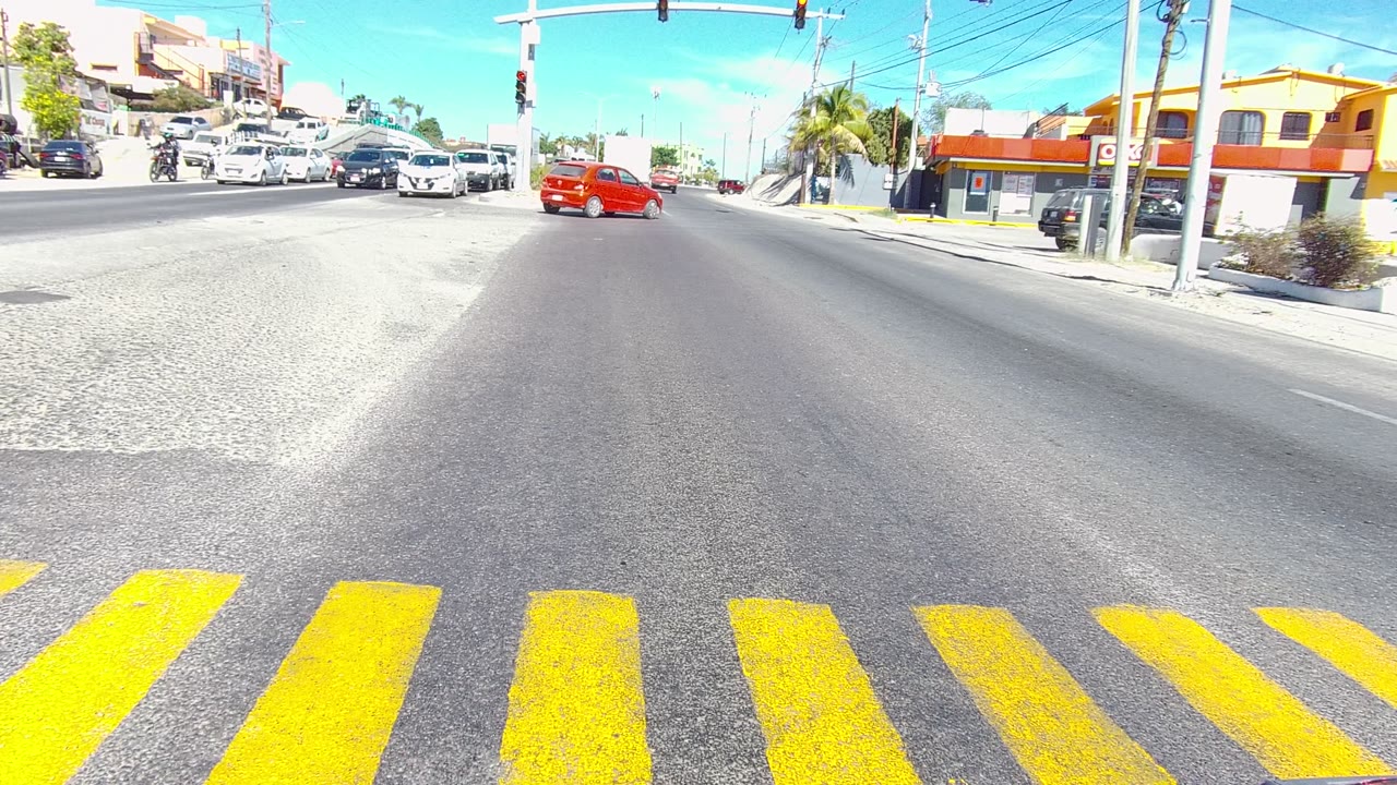 Red car moving through a city intersection under traffic lights.