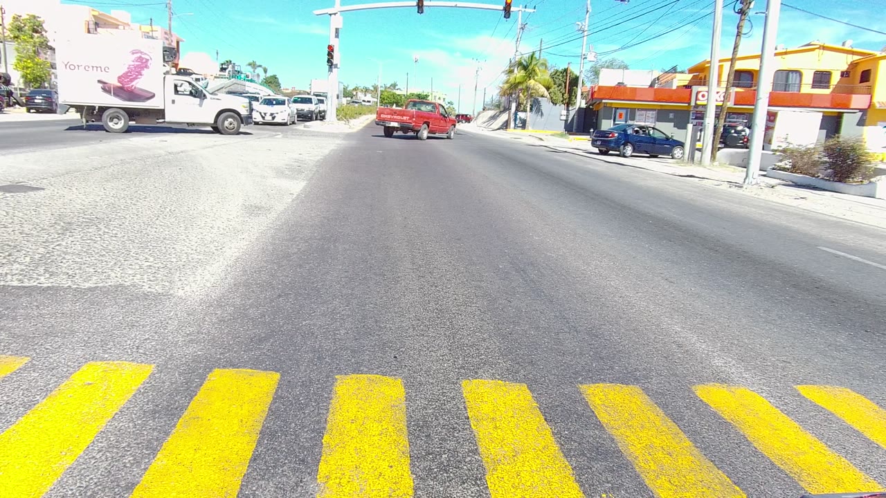 White box truck and red pickup moving through a sunlit intersection.