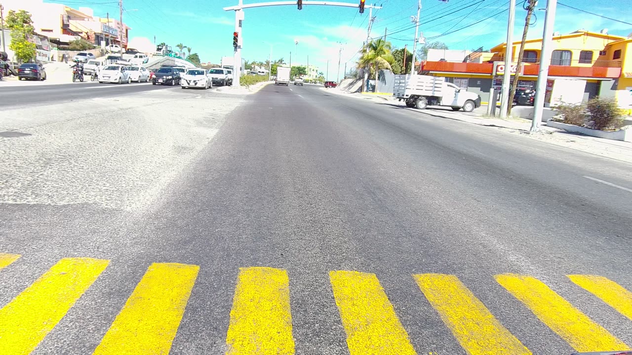Blue car crossing a bright intersection with yellow crosswalk stripes.