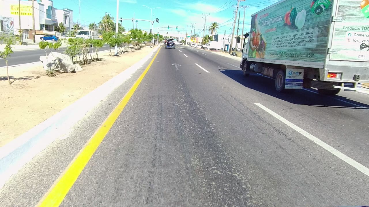 Straight paved road with a truck ahead to the right and commercial buildings beyond.