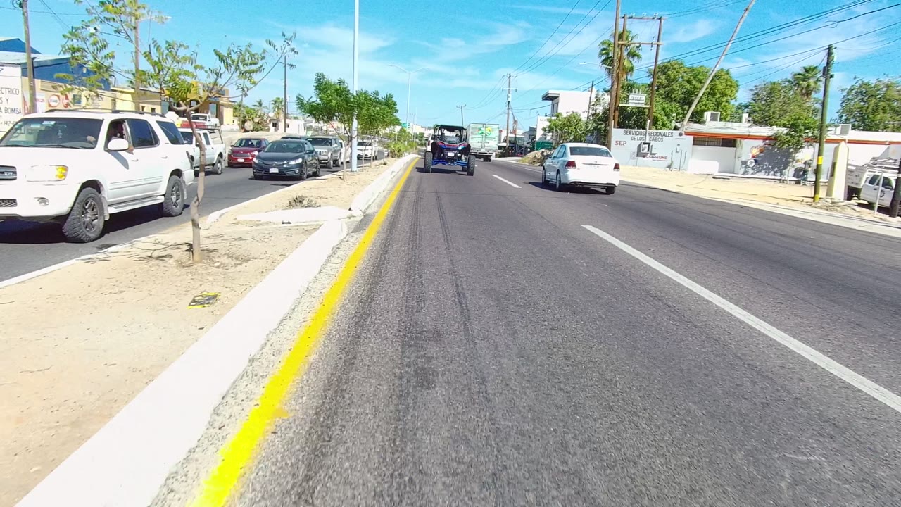 Roadway passing parked white pickup, cars, sidewalk, and utility poles.