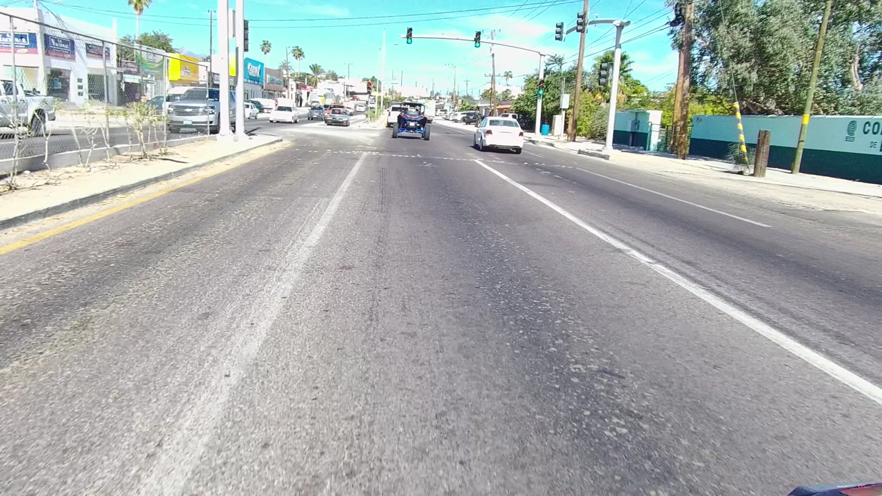 Urban road approach with cars ahead and commercial buildings along both sides.