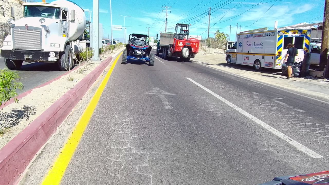 Roadway passing a white truck, ambulance-style vehicle, blue off-road vehicle, and red truck.