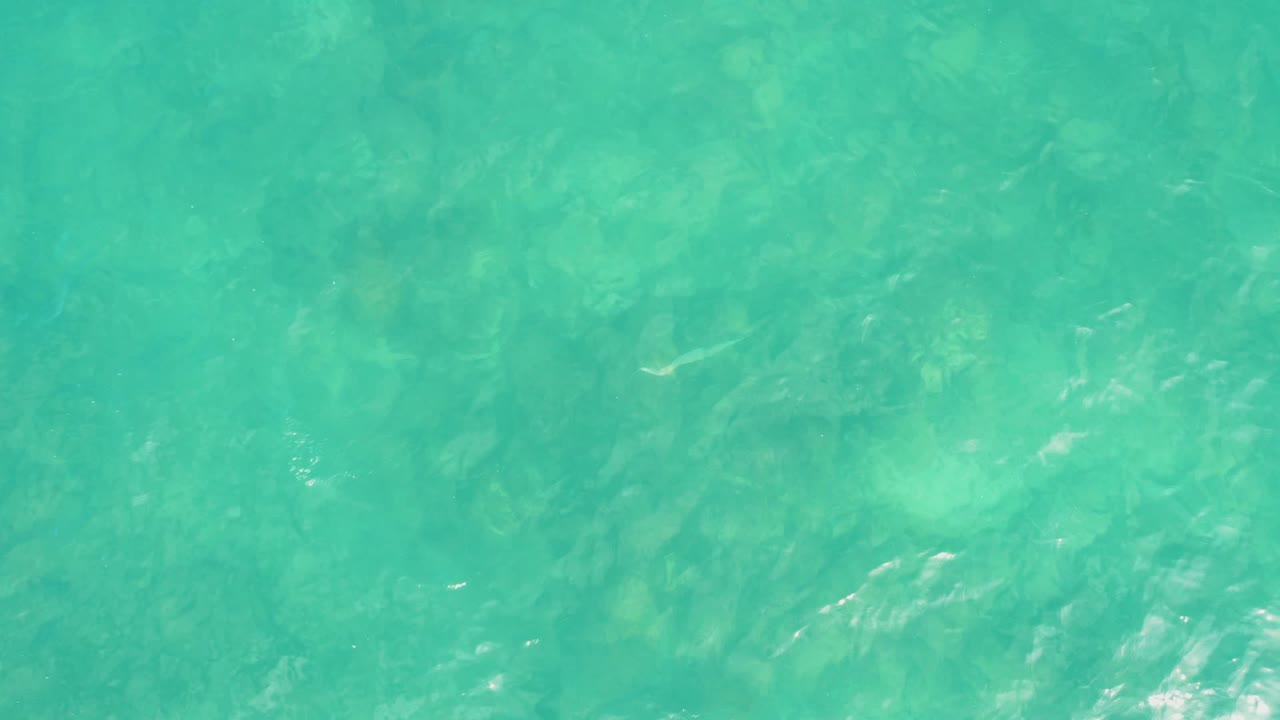 Clear turquoise ocean water at El Tule Los Cabos with muted seabed shapes visible beneath light ripples and no visible people.