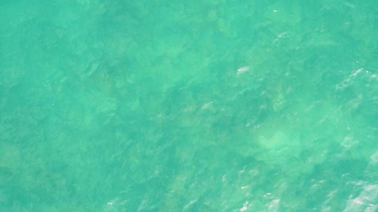 Turquoise water with faint underwater rock or sand patterns.