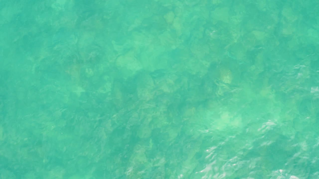 Rippling clear water over pale seabed areas at El Tule Los Cabos, with the frame filled entirely by ocean and no visible people.